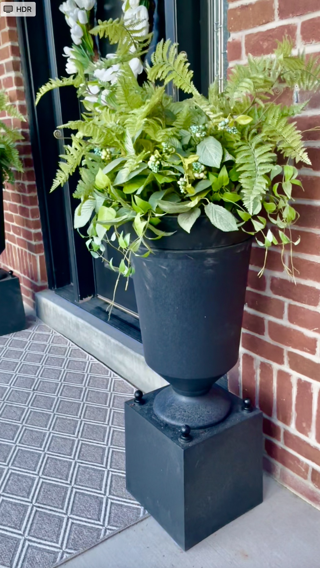 Tall black Estate Style Planter created from two pots. A square planter is turned upside down to create a base, with a round, cylindrical planter placed on top. Stacking the two together creates the illusion of a single, large planter.